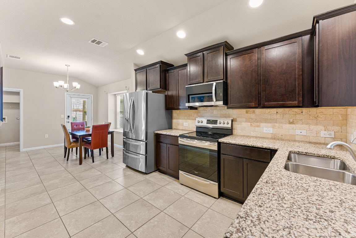 408 Cane River Road Pflugerville, TX 78660 - Photo 6 of 38 a kitchen with granite countertop a table chairs microwave and refrigerator