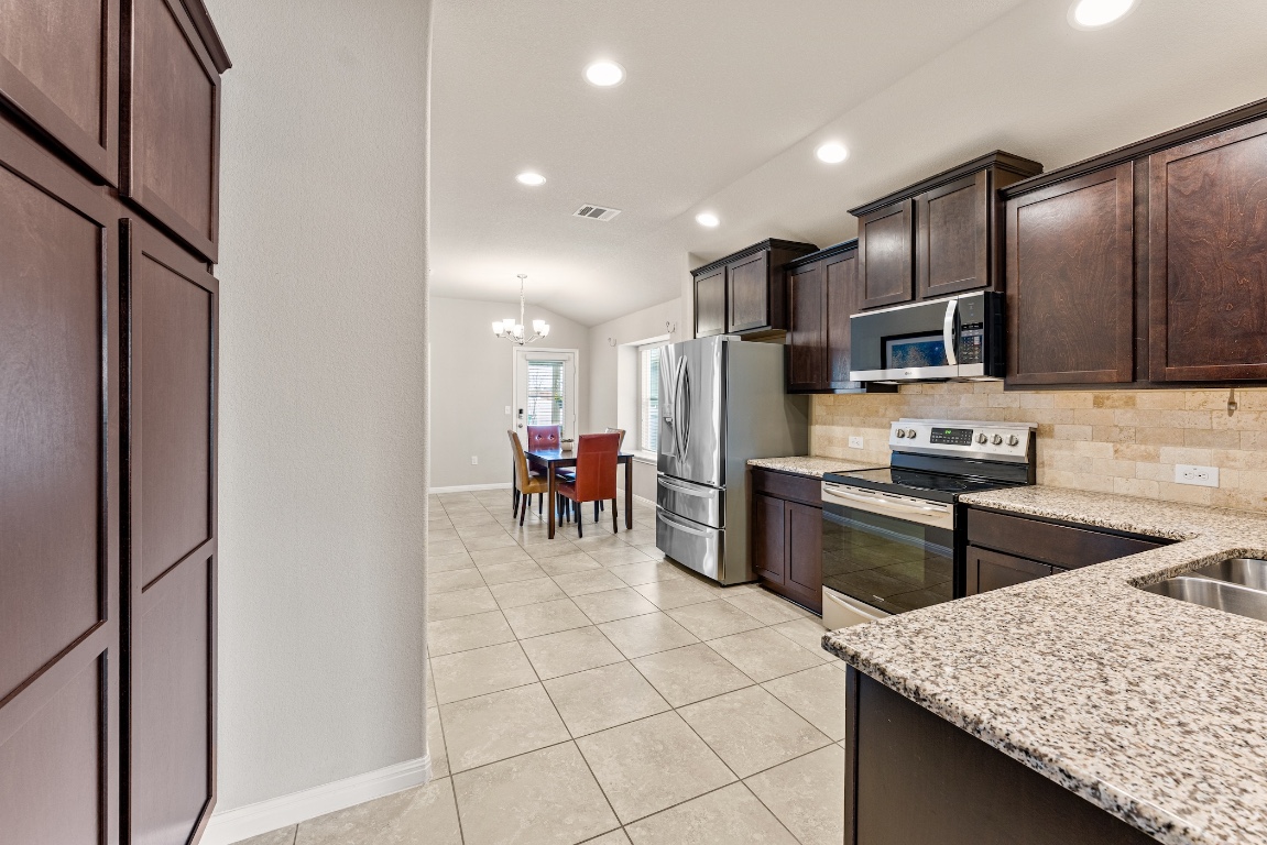 408 Cane River Road Pflugerville, TX 78660 - Photo 7 of 38 a kitchen with stainless steel appliances kitchen island granite countertop a refrigerator and a stove top oven