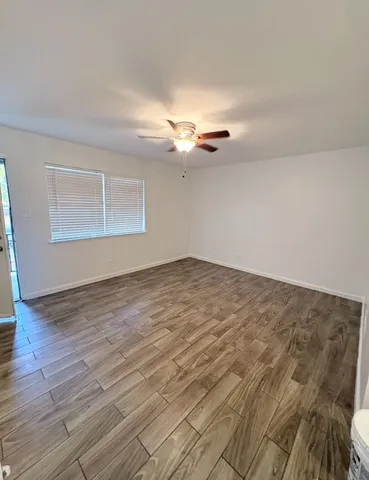 an empty room with wooden floor fan and windows