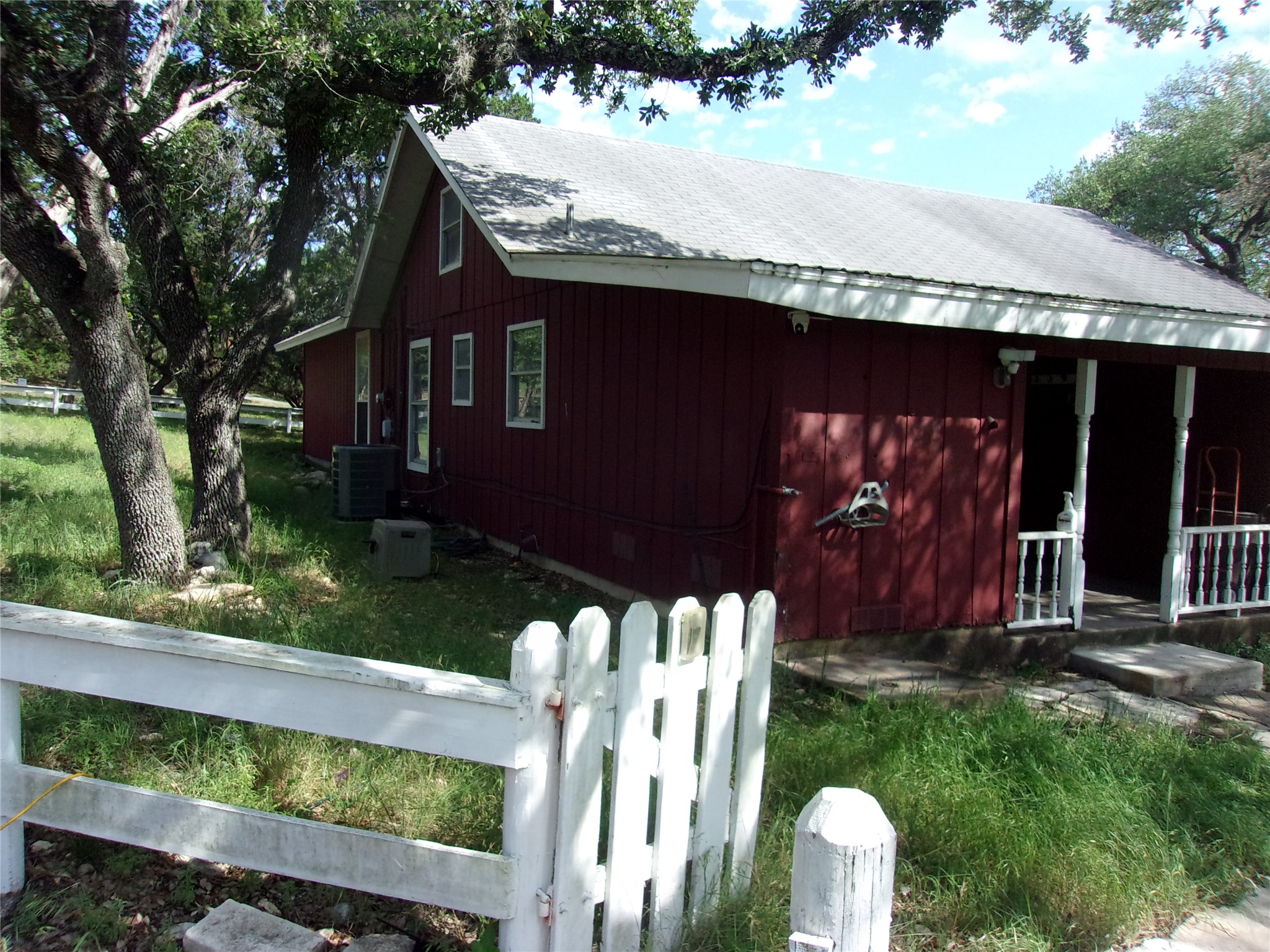 702 Cottonwood Creek Road Dripping Springs, TX 78620 - Photo 23 of 31 Red vertical siding exterior with white trim, a covered front porch, and a white picket fence