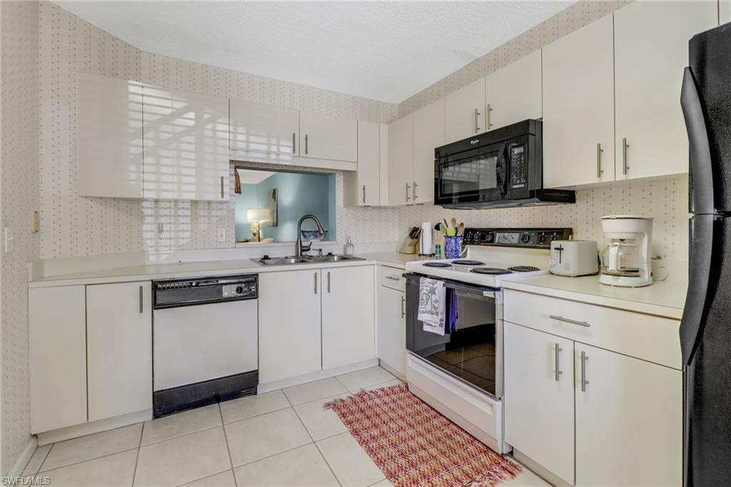 7791 Esmeralda Way, Unit L103 Naples, FL 34109 - Photo 8 of 46 a kitchen with white cabinets and appliances