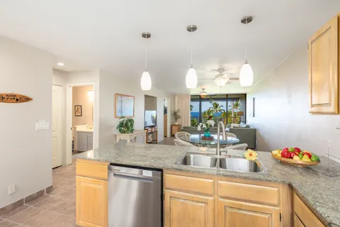 a kitchen with kitchen island granite countertop a sink cabinets and living room view