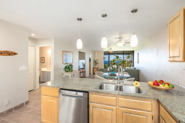 a kitchen with kitchen island granite countertop a sink cabinets and living room view