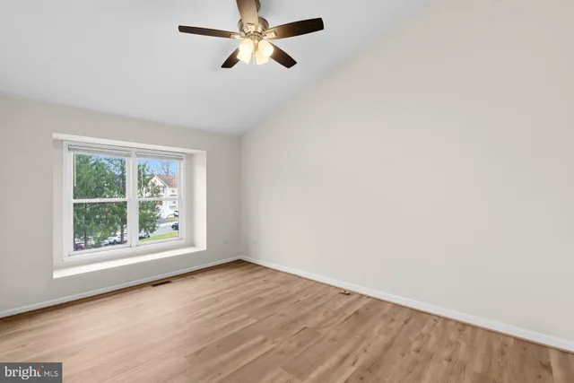 an empty room with wooden floor fan and windows