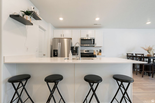 1693 Devils Gdn Lane Washington, UT 84780 - Photo 10 of 64 Modern kitchen featuring white cabinetry, stainless steel appliances, a breakfast bar, recessed lighting, and light wood-finish flooring