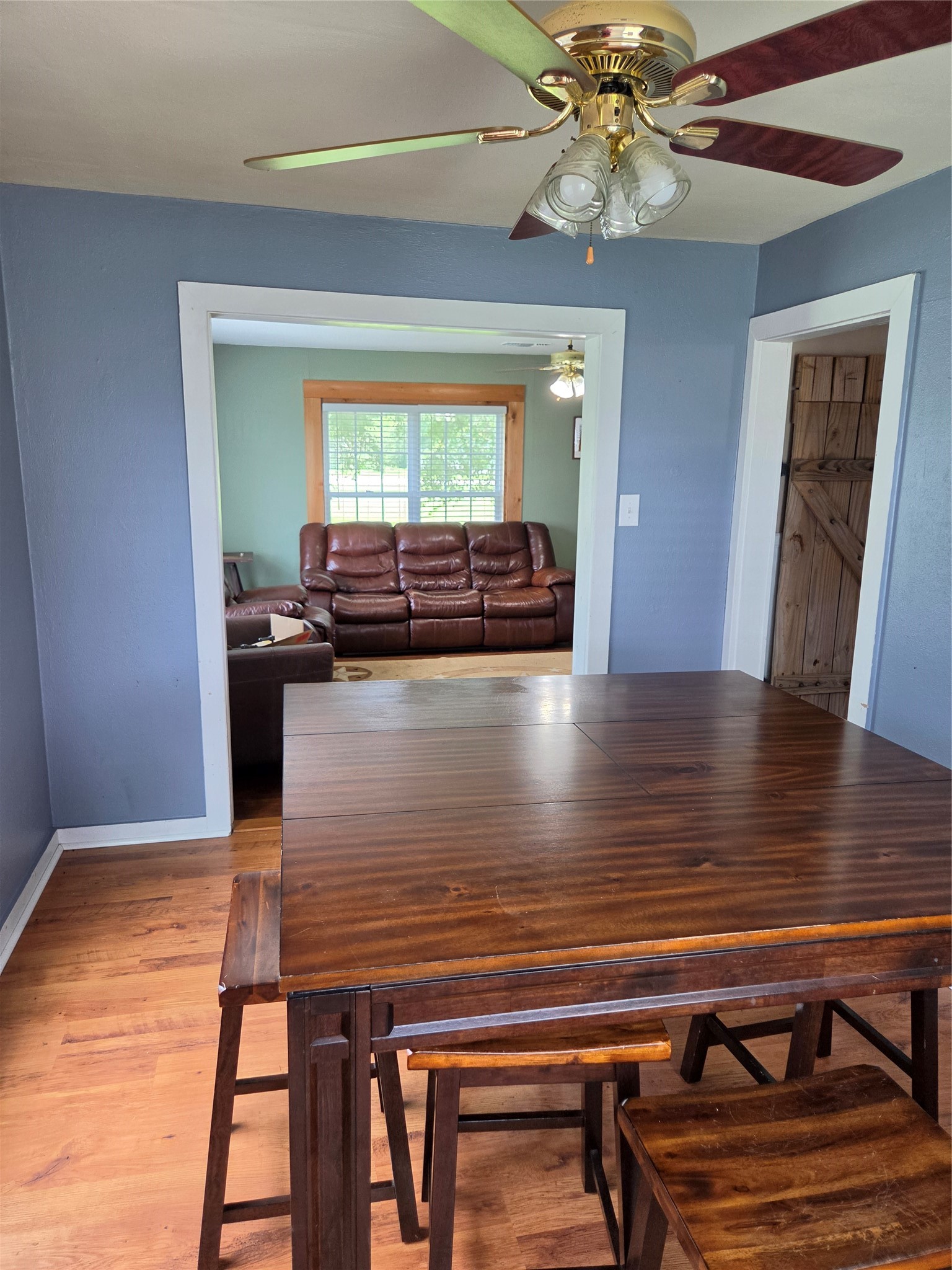 4910 FM 3012 Road Wharton, TX 77488 - Photo 6 of 21 Cozy dining area, adjacent to a living room. The space has hardwood floors, light blue walls, and ceiling fans in both rooms, providing a welcoming atmosphere.