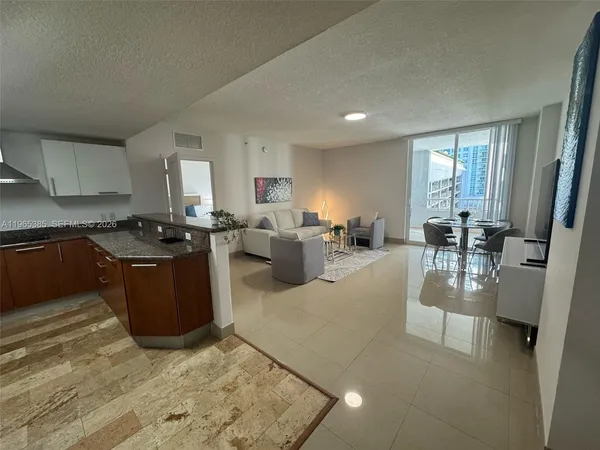 a kitchen with stainless steel appliances granite countertop a stove a sink a refrigerator white cabinets and couches with wooden floor