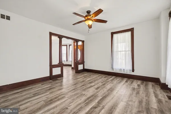 an empty room with wooden floor chandelier fan and windows