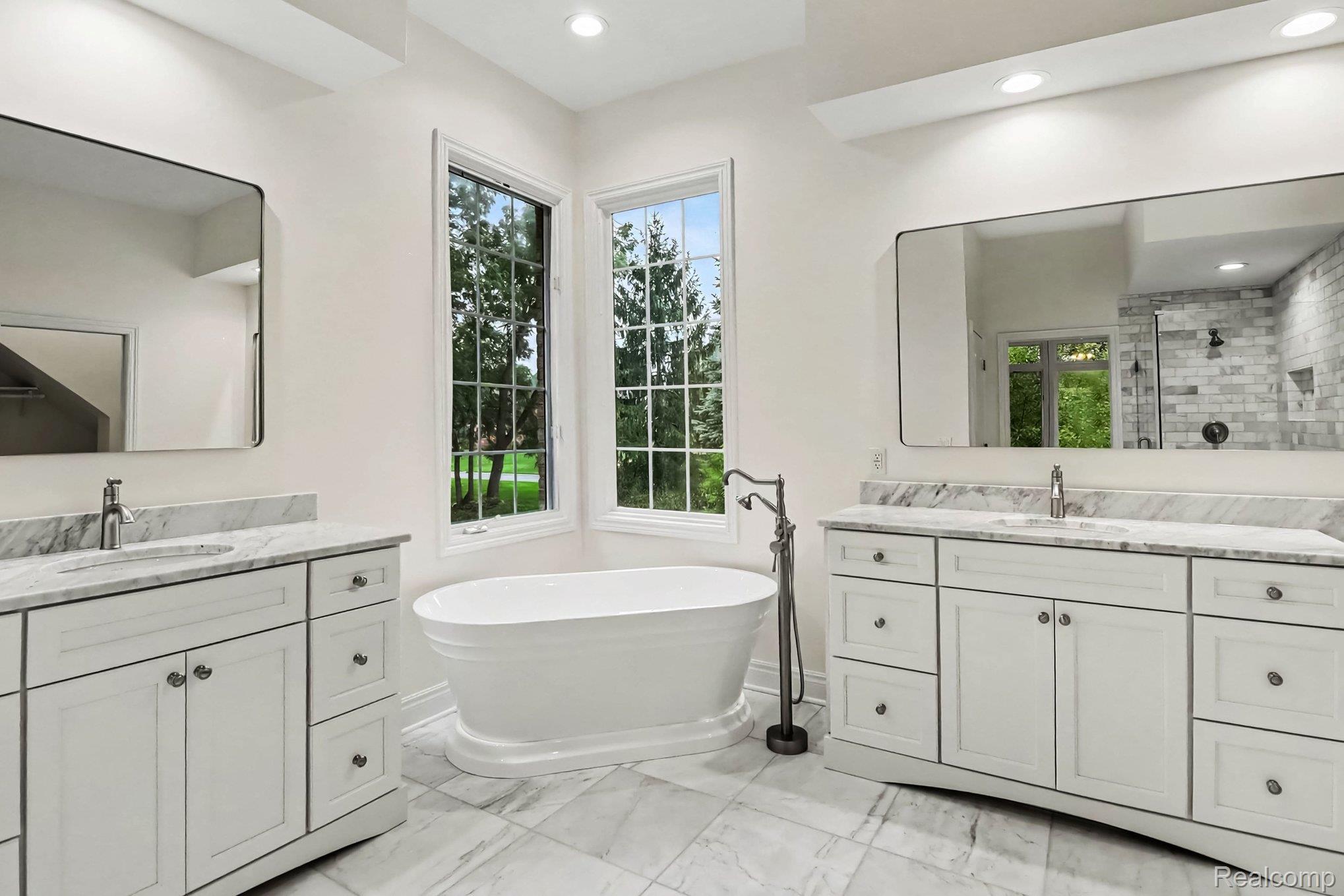 4875 Green Meadow Lane Rochester, MI 48306 - Photo 42 of 60 Freestanding soaking tub with a floor-mounted faucet, dual vanities with stone countertops, and large windows