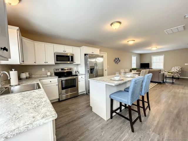 a kitchen with stainless steel appliances granite countertop a stove top oven a sink dishwasher a dining table and chairs with wooden floor