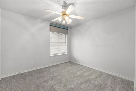 an empty room with a chandelier fan and windows
