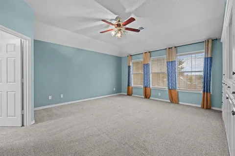 an empty room with chandelier fan and windows