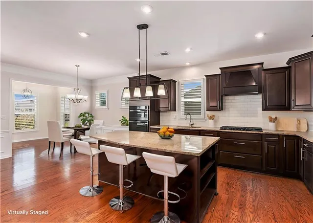 a kitchen with stainless steel appliances granite countertop a stove top oven a sink dishwasher a dining table and chairs with wooden floor