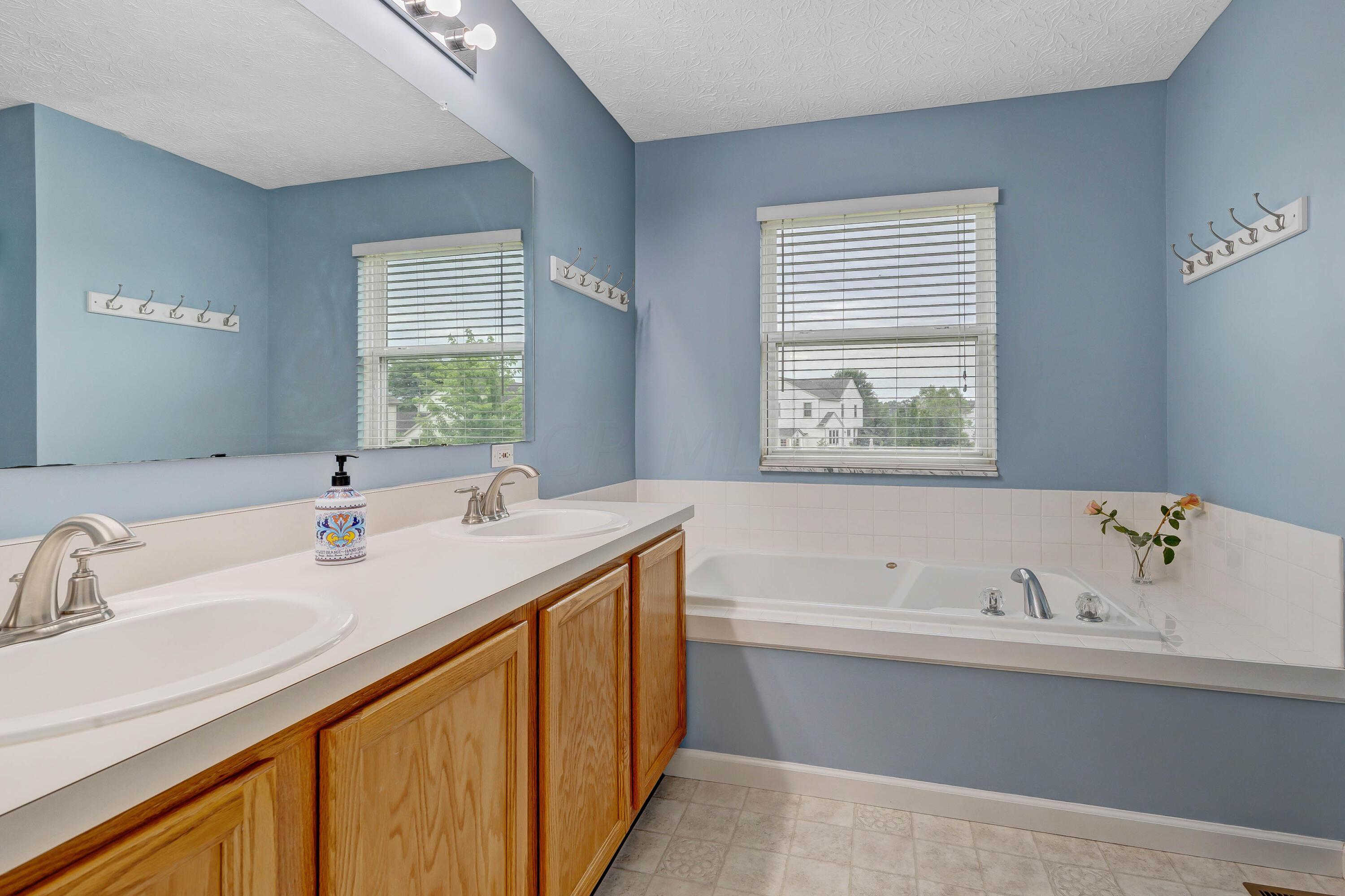 2136 Reeves Avenue Lewis Center, OH 43035 - Photo 31 of 57 • Neutral vinyl flooring • Blue painted walls • Shower stall with glass doors & ceramic tile surround • Garden tub with ceramic tile surround • Ceiling exhaust • Studio lighting strip • Mirrored medicine cabinet • Enclosed vanity with double bowl sinktop • 2” blinds