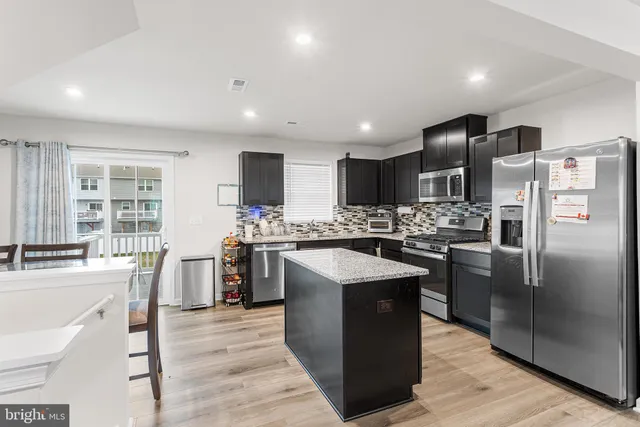 a kitchen with stainless steel appliances kitchen island granite countertop a refrigerator a sink dishwasher a oven with white cabinets and wooden cabinets