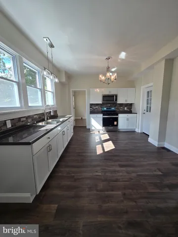 a kitchen with kitchen island granite countertop a stove top oven a chimney cabinets and wooden floor