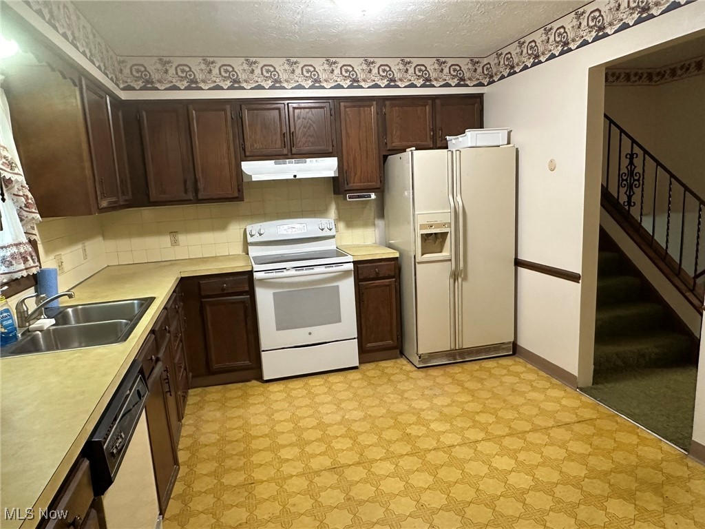 97 West Howe Road Tallmadge, OH 44278 - Photo 24 of 35 Kitchen with sink, white appliances, dark brown cabinetry, a textured ceiling, and decorative backsplash