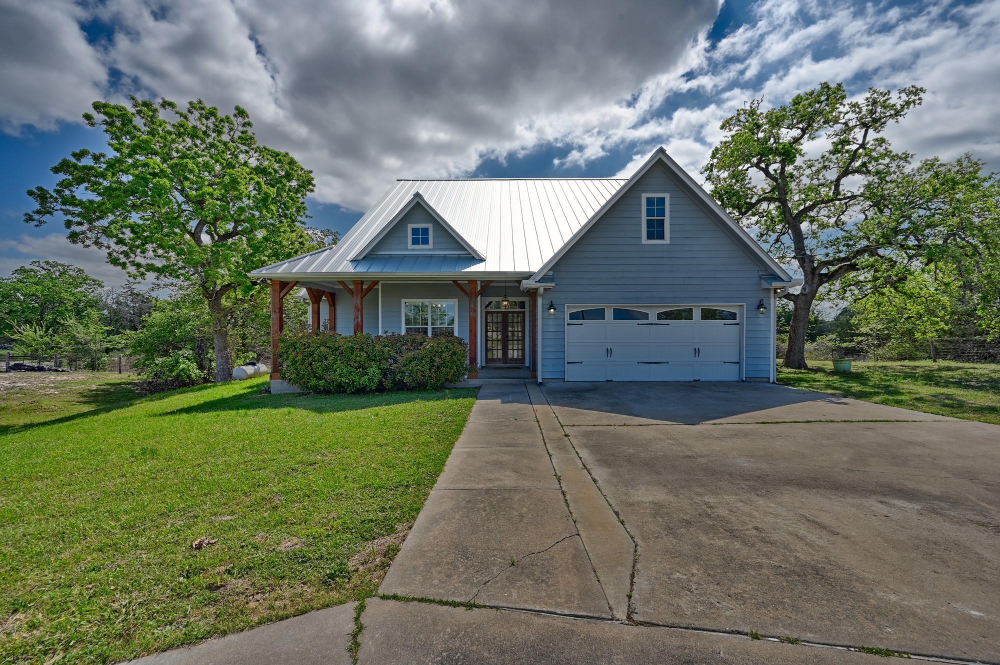 350 Owl Creek Road Giddings, TX 78942 - Photo 5 of 29 View of front of house featuring a front lawn, a porch, concrete driveway, and a standing seam roof