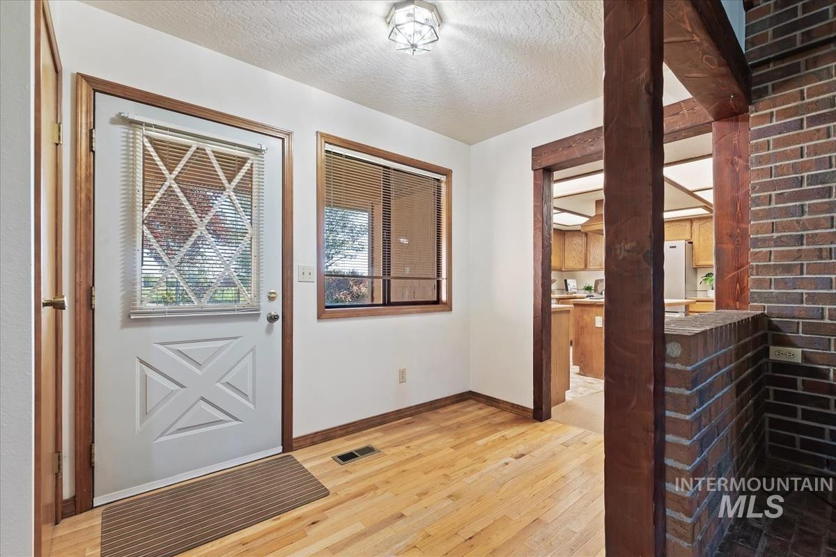 8275 Washoe Road Fruitland, ID 83619 - Photo 8 of 43 Hardwood flooring, brick accent wall, wood trim, white entry door with decorative glass, and recessed window