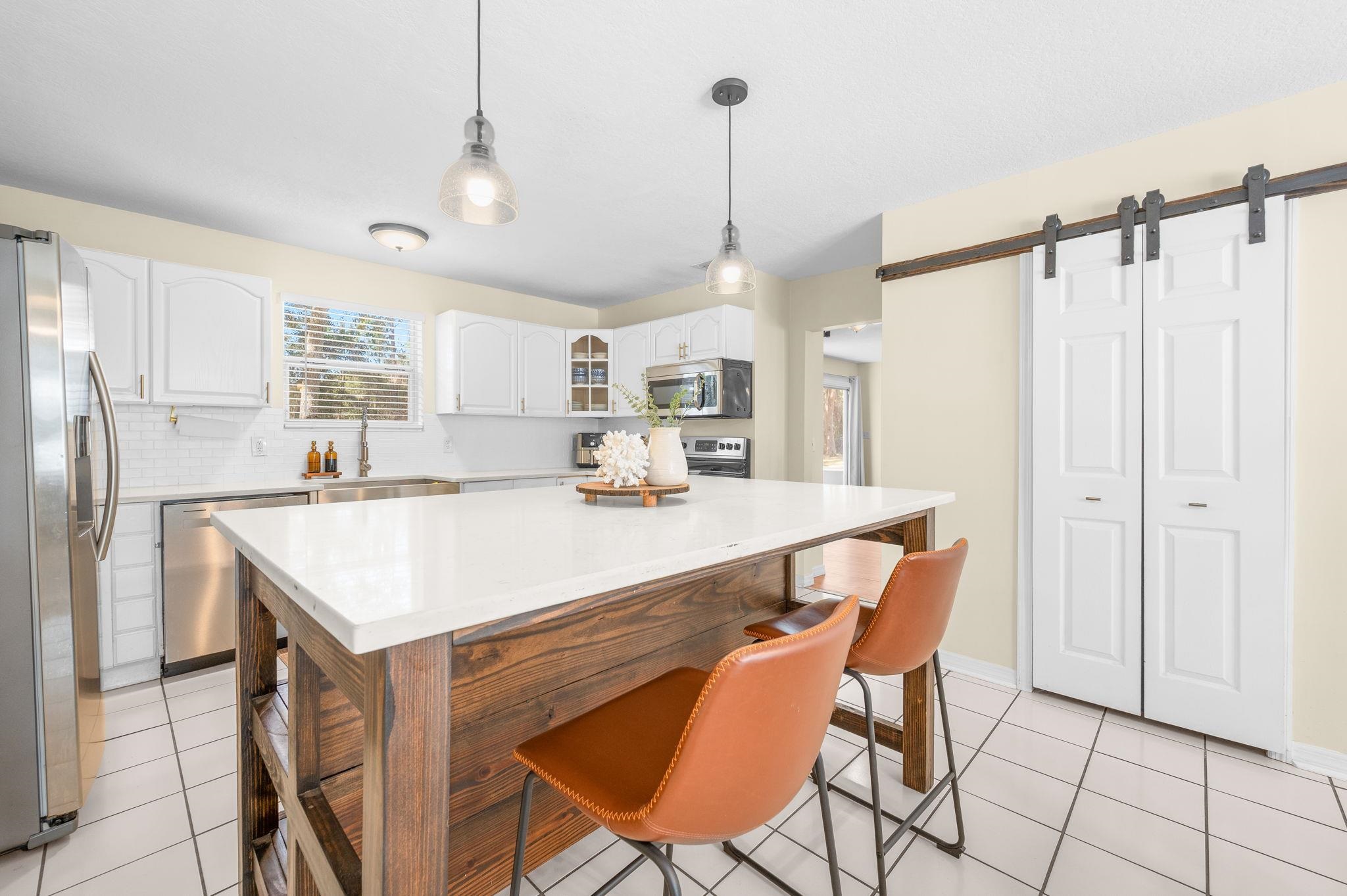 4233 Oak Lane St. Augustine, FL 32086 - Photo 22 of 42 Kitchen featuring a barn door, white cabinetry, hanging light fixtures, stainless steel appliances, and glass insert cabinets