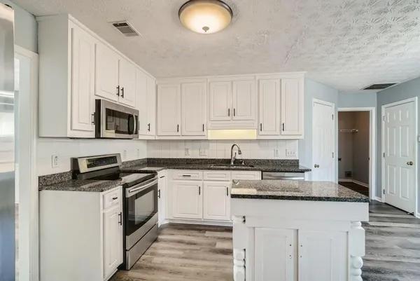 a kitchen with granite countertop white cabinets stainless steel appliances and a counter space