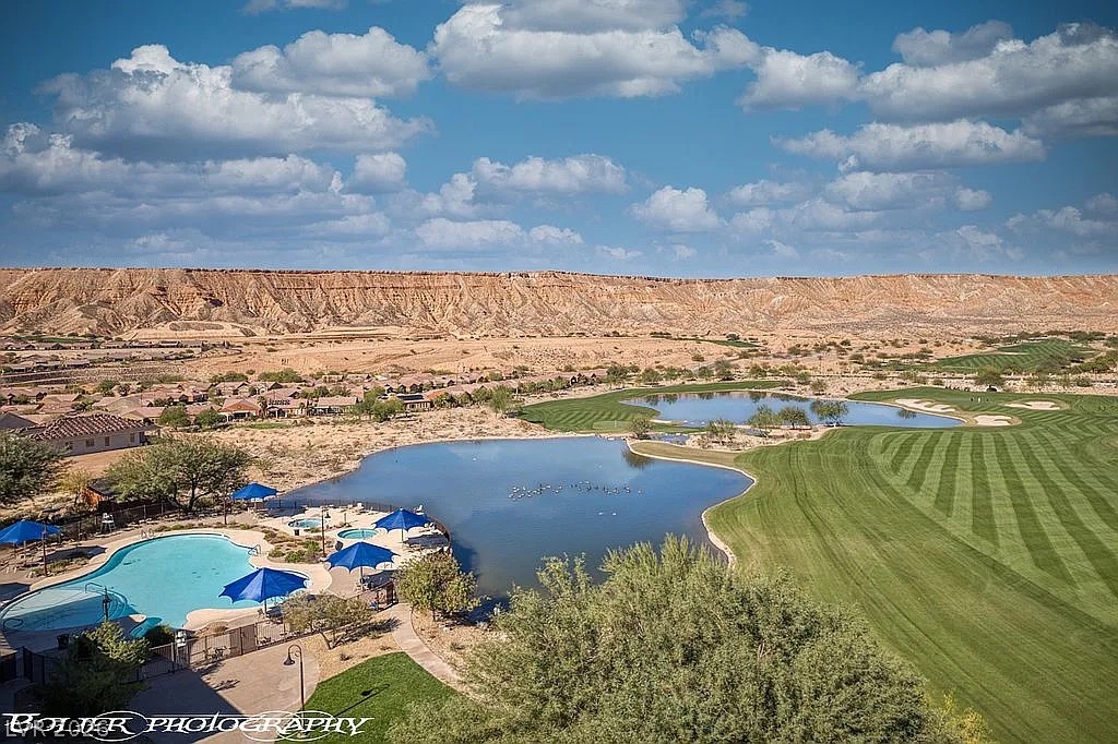 1304 Cottage Ridge Mesquite, NV 89034 - Photo 50 of 52 An aerial perspective reveals a vibrant golf course, tranquil lake, and a welcoming pool area set against a dramatic desert mountain range.