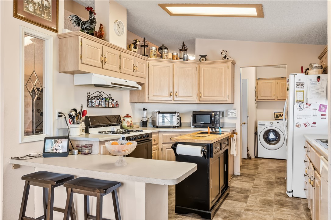1545 East El Rodeo Road, Unit 58 Fort Mohave, AZ 86426 - Photo 14 of 47 Kitchen featuring light brown cabinets, gas range, a kitchen bar, freestanding refrigerator, and washer / clothes dryer