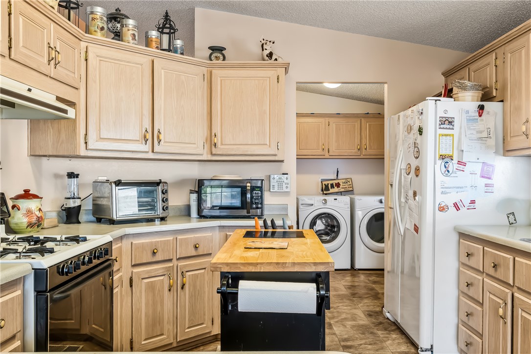 1545 East El Rodeo Road, Unit 58 Fort Mohave, AZ 86426 - Photo 15 of 47 Kitchen with white appliances, independent washer and dryer, vaulted ceiling, light brown cabinetry, and a textured ceiling