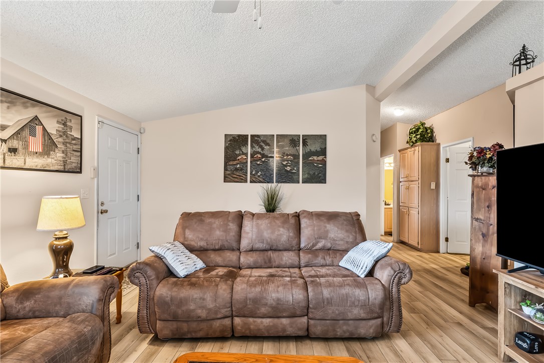 1545 East El Rodeo Road, Unit 58 Fort Mohave, AZ 86426 - Photo 10 of 47 Living area featuring lofted ceiling, a textured ceiling, a ceiling fan, and light wood-style flooring