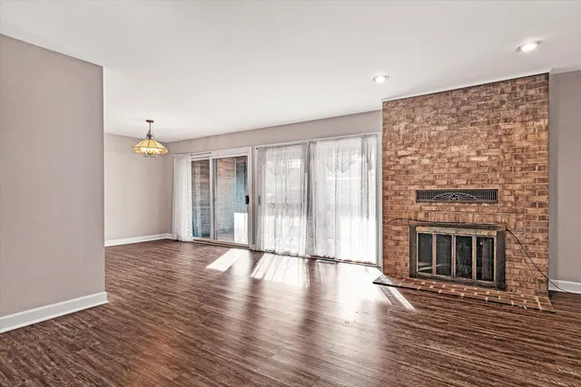 a view of an empty room with wooden floor fireplace and a window