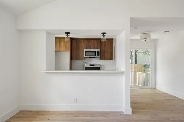 a living room with stainless steel appliances wooden floor and view kitchen