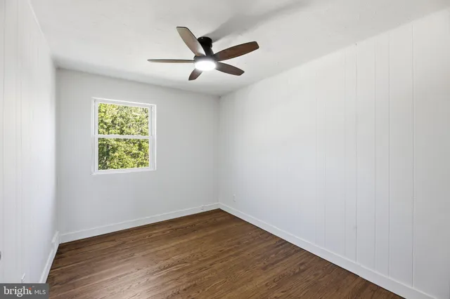 an empty room with wooden floor ceiling fan and window