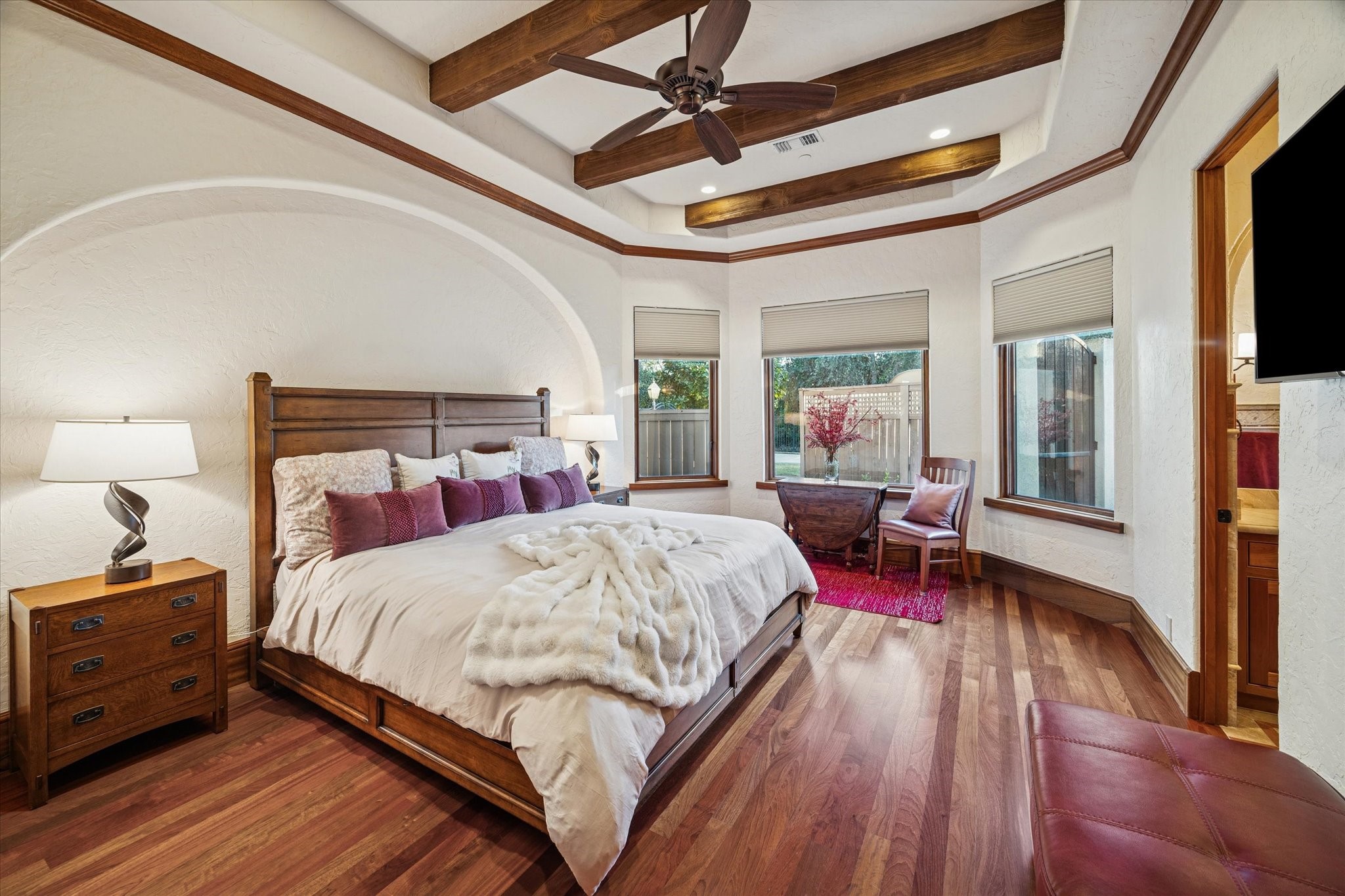 21538 Mueschke Road Tomball, TX 77377 - Photo 32 of 50 Secondary bedroom with a beautiful window that fills the space with natural light, featuring direct access to a private en-suite bathroom for added privacy and convenience. Elegant wood beam accents on the ceiling and a graceful arch reflect a rustic Mediterranean style with a contemporary touch, creating a comfortable and sophisticated retreat for your loved ones.