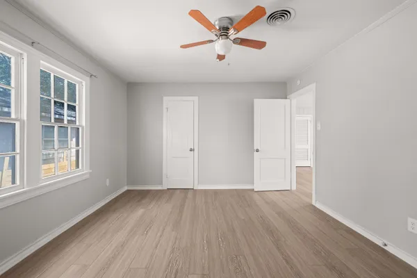 an empty room with wooden floor chandelier fan and windows