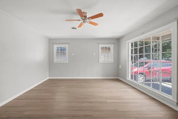 a view of an empty room with wooden floor and a ceiling fan