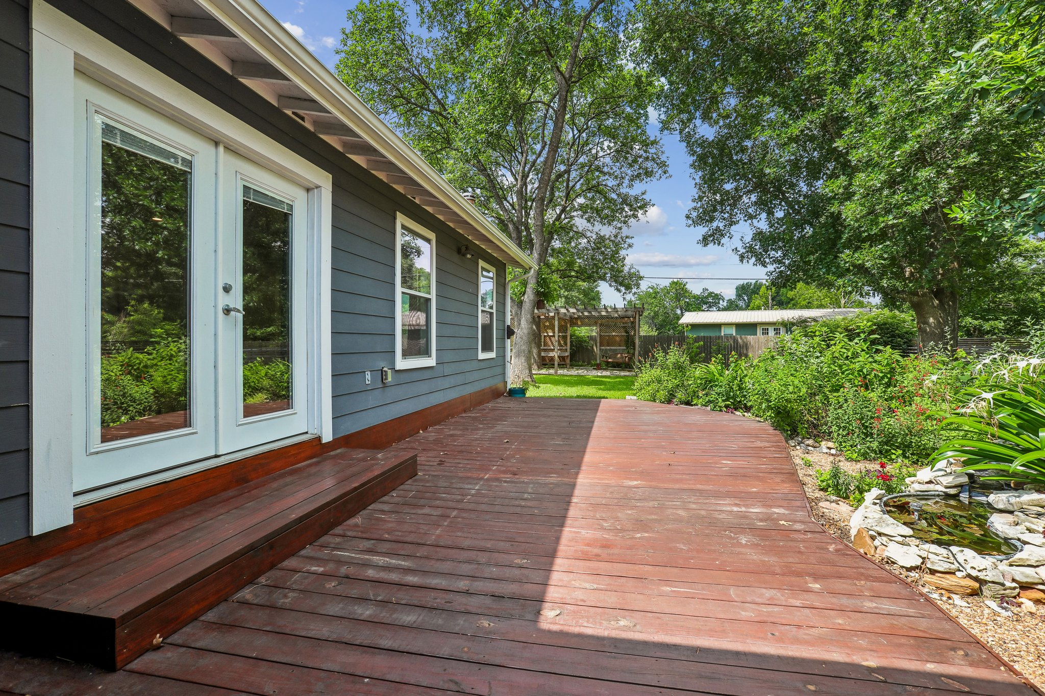 1114 West 2nd Street Elgin, TX 78621 - Photo 22 of 31 A spacious wooden deck extends from the residence, bordered by lush garden beds and a serene pond.