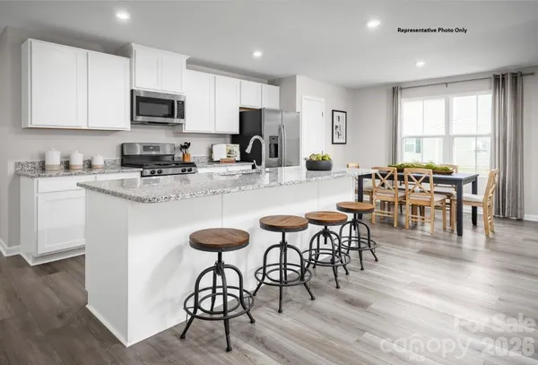 a kitchen with stainless steel appliances granite countertop a stove a sink a microwave a dining table and chairs with wooden floor