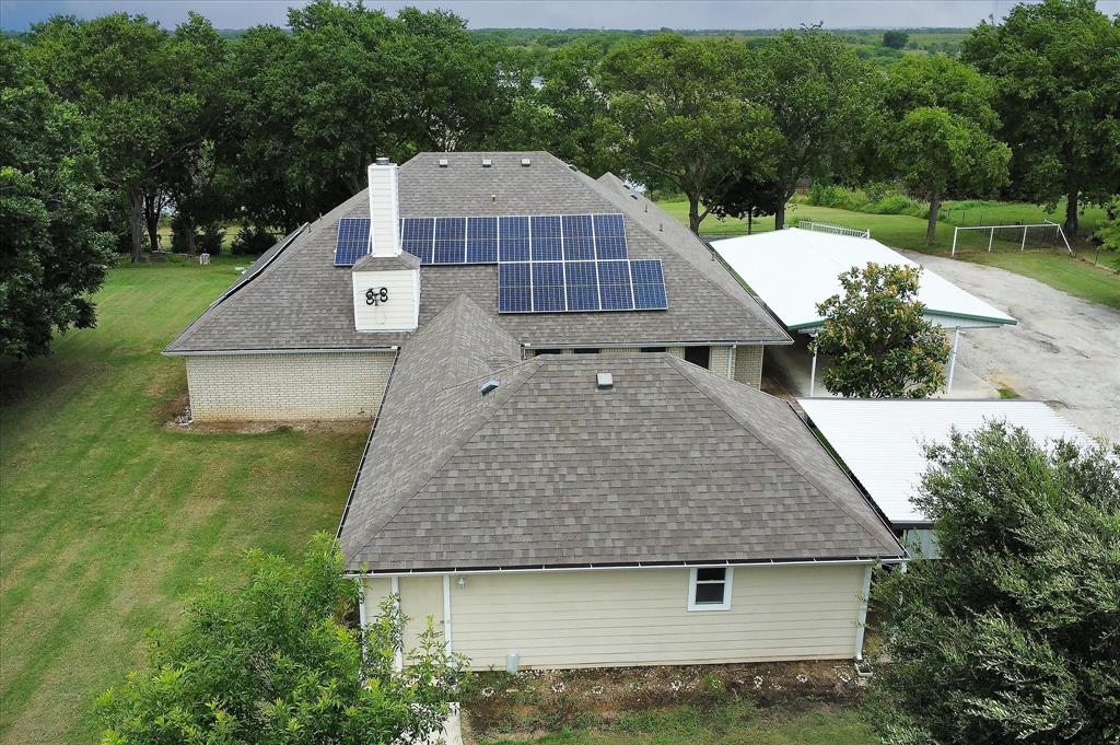 3007 McReynolds Road Sanger, TX 76266 - Photo 39 of 39 Shingle roof with integrated solar panels, brick and siding exterior, white chimney, and two white metal outbuildings