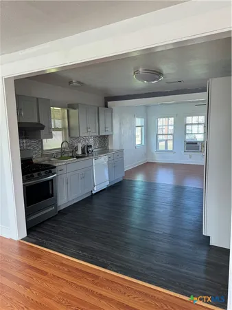 a view of an empty room with wooden floor and a kitchen