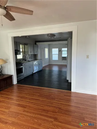 a view of empty room with wooden floor and kitchen view