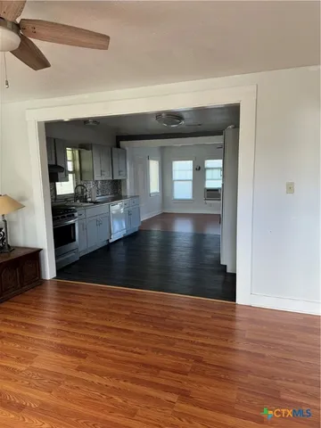 a view of empty room with wooden floor and kitchen view