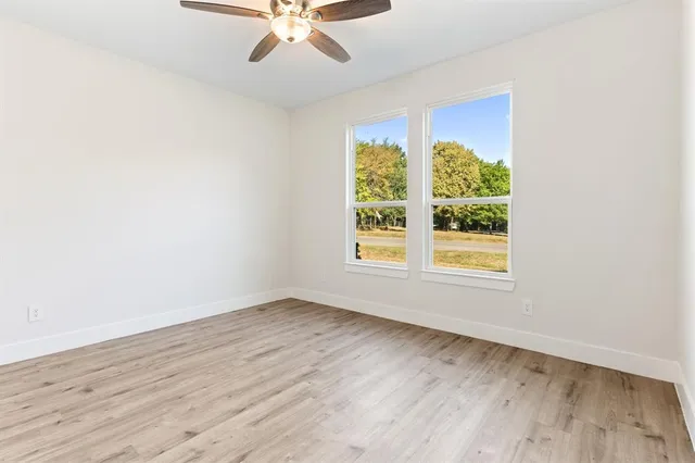 an empty room with wooden floor fan and windows