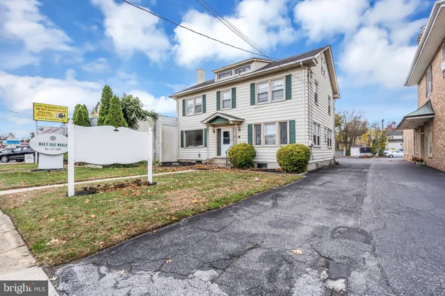 a view of a white house next to a yard with big trees