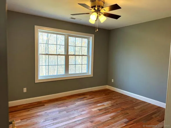 an empty room with wooden floor fan and windows