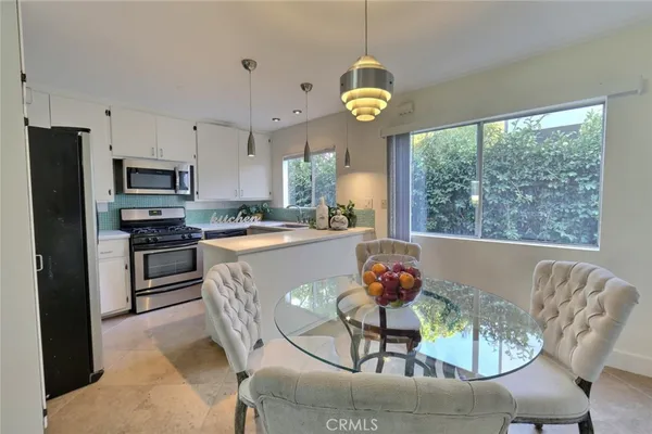 a kitchen with stainless steel appliances granite countertop a stove a refrigerator a microwave a dining table and chairs with wooden floor