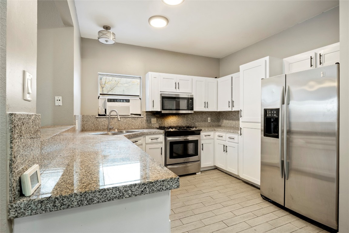 16801 Gravesend Road Pflugerville, TX 78660 - Photo 7 of 30 Kitchen featuring appliances with stainless steel finishes, white cabinetry, light stone countertops, wood tiled floors, and tasteful backsplash