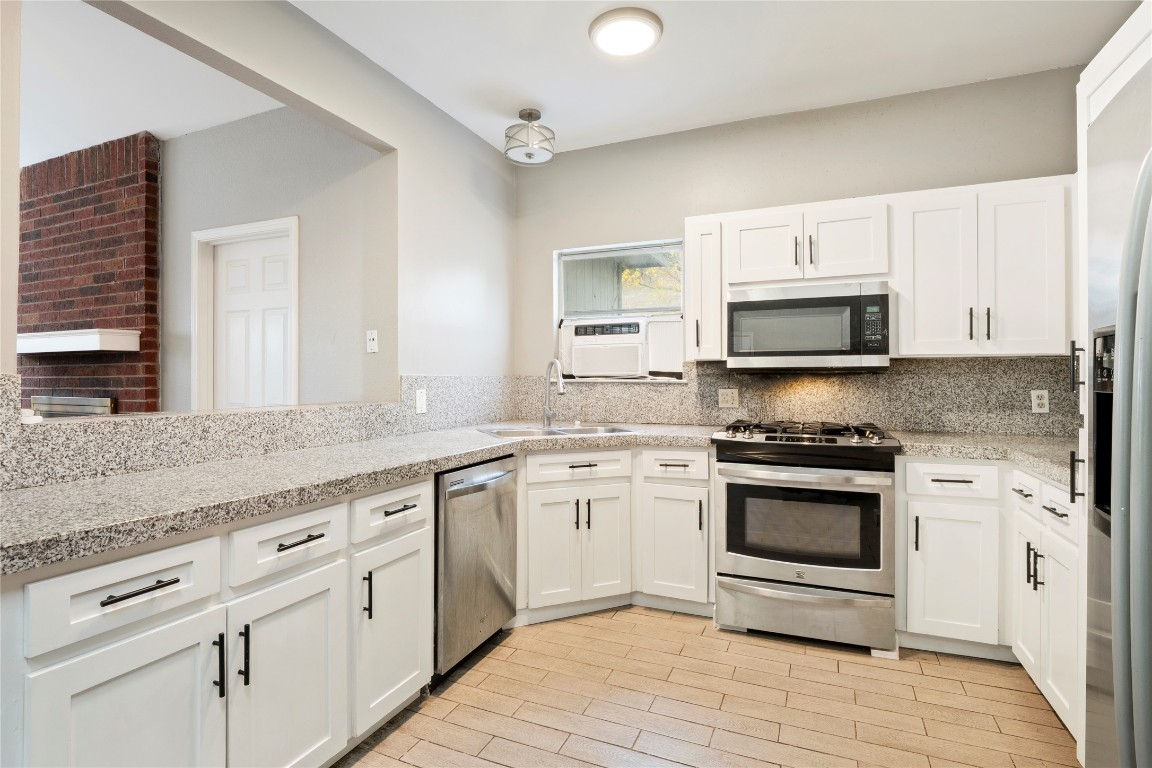 16801 Gravesend Road Pflugerville, TX 78660 - Photo 8 of 30 Kitchen featuring appliances with stainless steel finishes, white cabinetry, light stone countertops, wood tiled floors, and tasteful backsplash