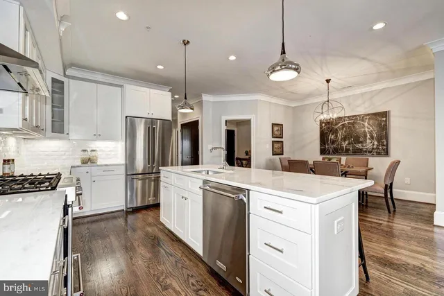 a kitchen that has a lot of white cabinets and stainless steel appliances