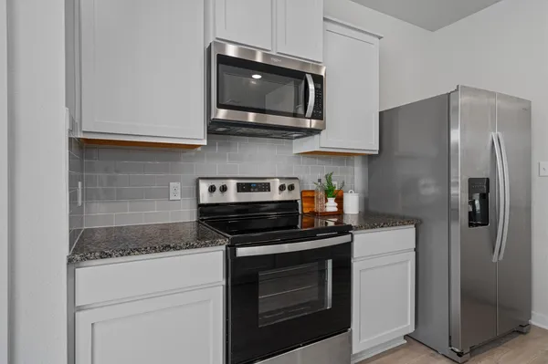 a kitchen with stainless steel appliances granite countertop white cabinets a stove a microwave and a refrigerator