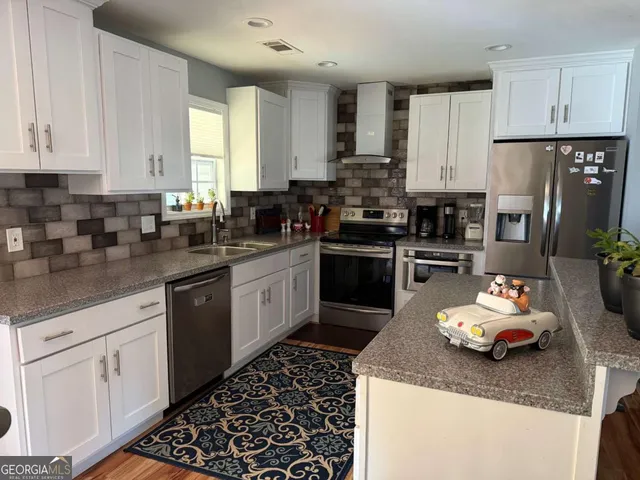 a kitchen with kitchen island granite countertop a sink dishwasher stove and white cabinets